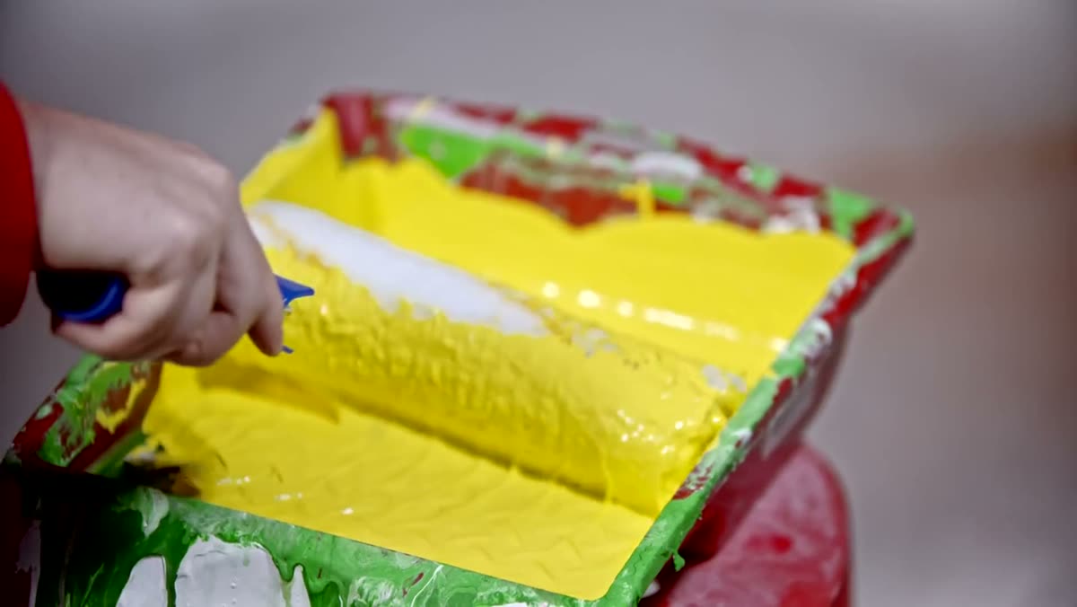 Paint roller loaded in a tray of bright yellow paint